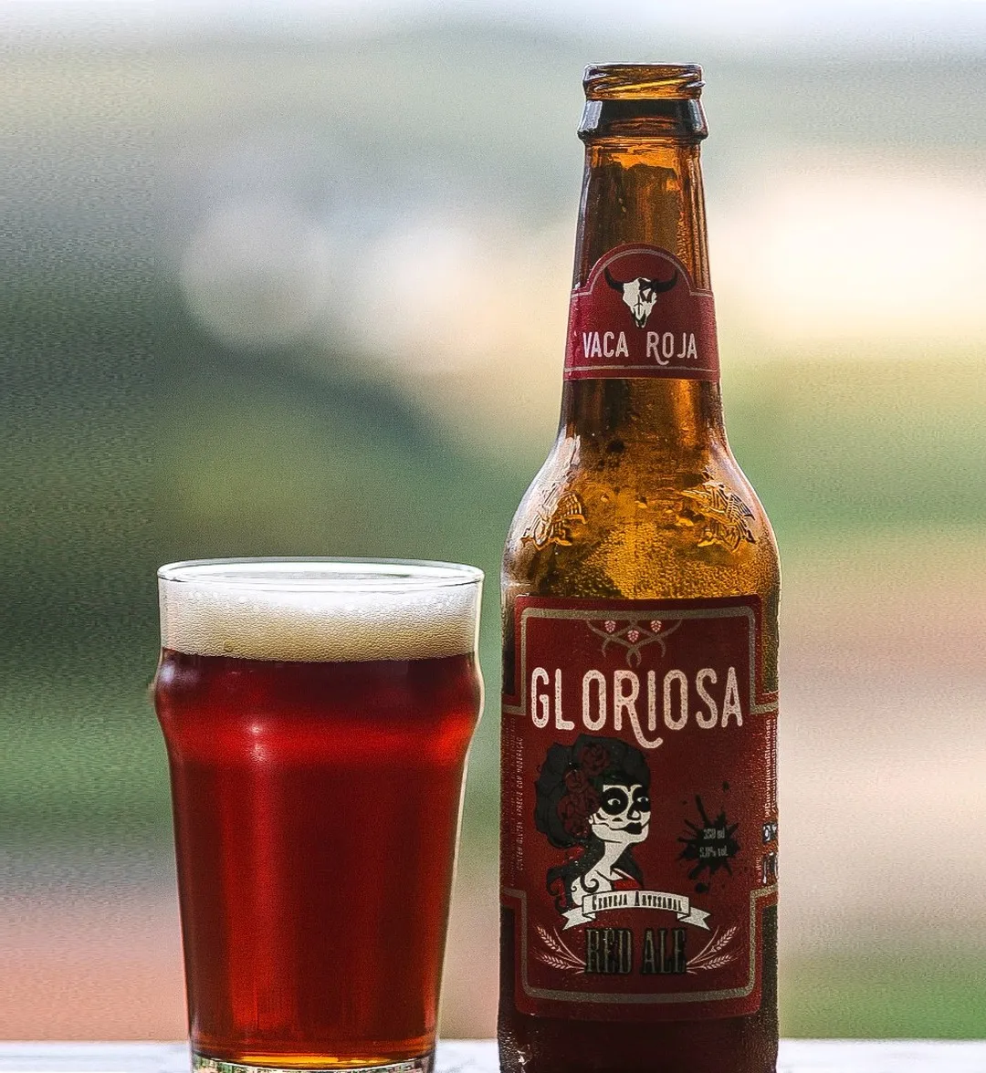 A bottle of Gloriosa’s Vaca Roja red ale next to a full pint glass of deep red beer